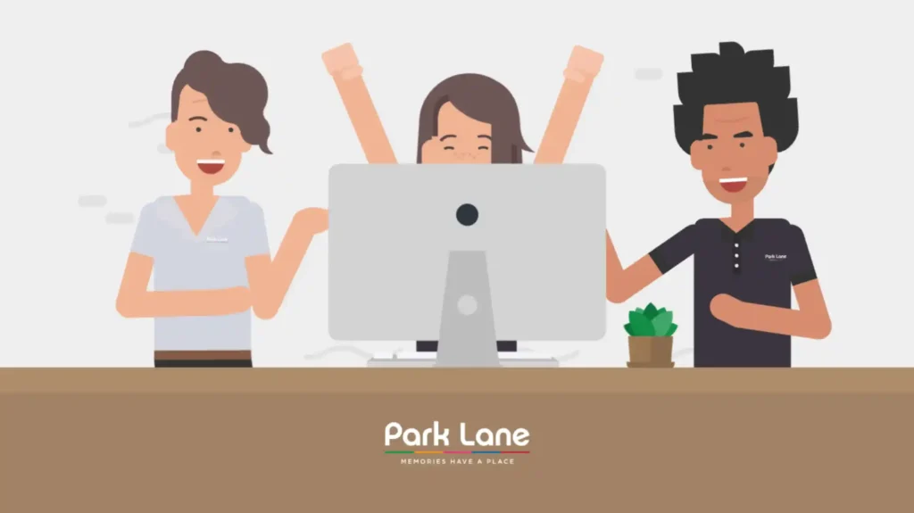 Three people behind a computer, smiling and celebrating. The desk has a plant and 